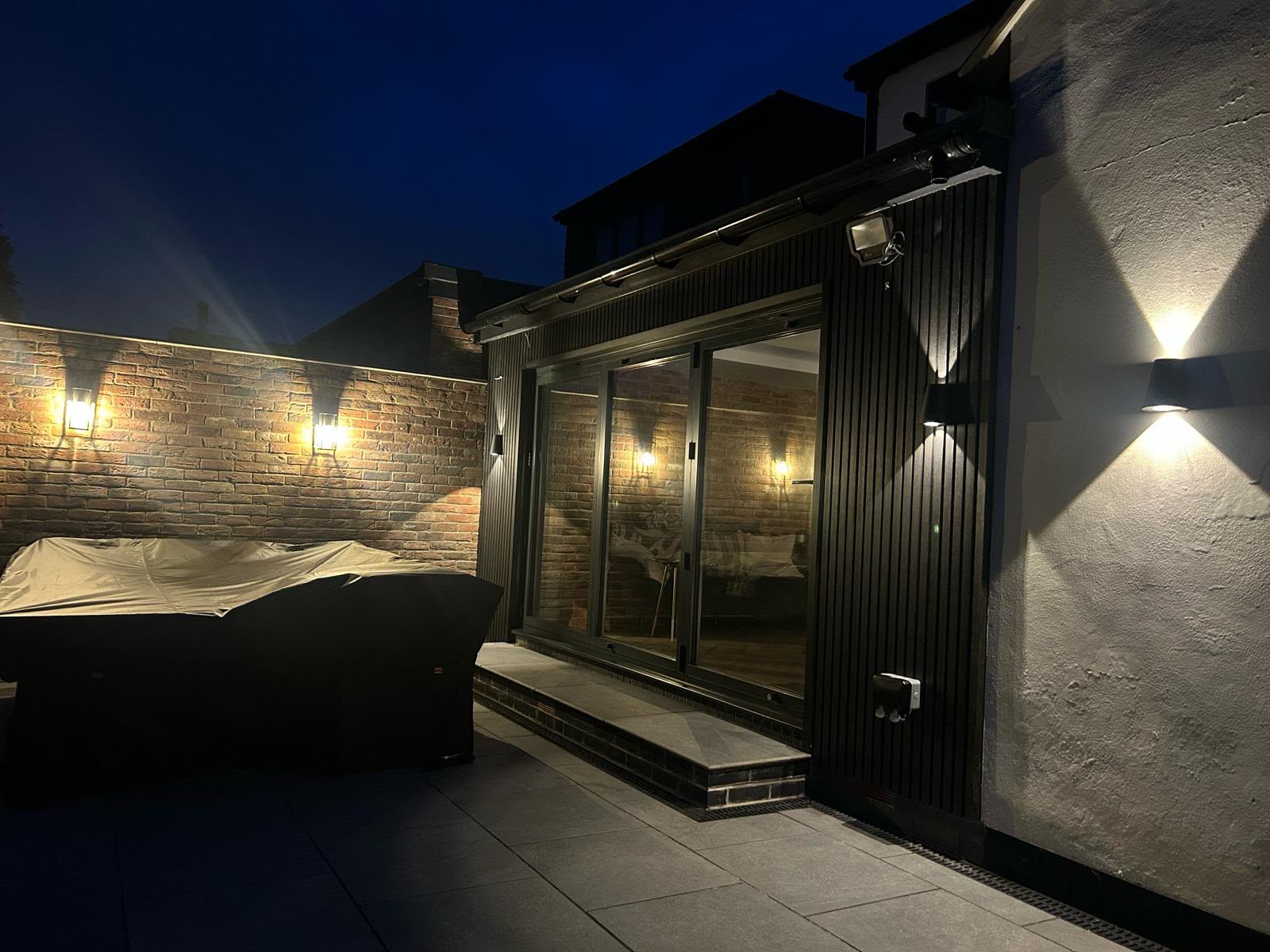 Completed rear extension at night with black slatted cladding, bifold doors and outdoor lighting